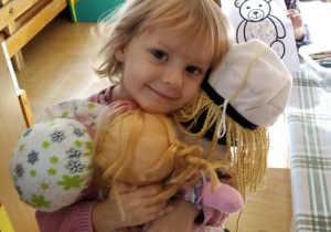 Dziewczynka trzyma lalki, w tle dziewczynka z malowanką.
